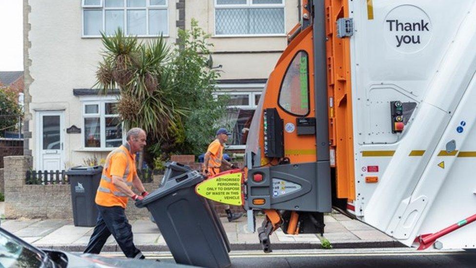 Binmen emptying black bins into waste collection lorry