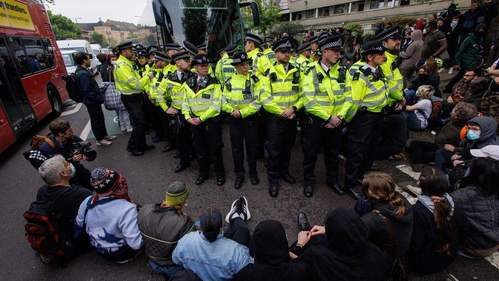 Police officers stand in front of a coach with people sat down in front of them