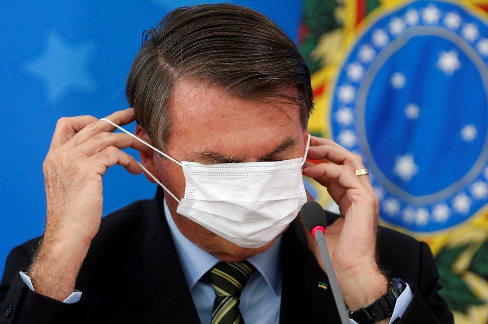 Brazil's President Jair Bolsonaro adjusts his protective face mask