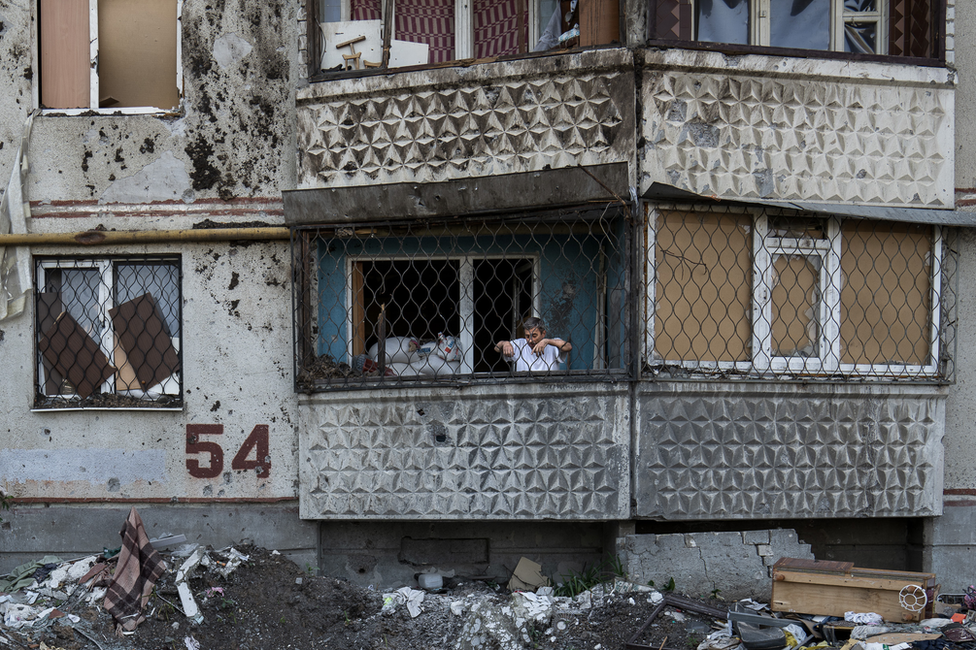 A resident of Saltivka building 54 looks down from his balcony at a shell crater beneath. "This is the Russian world," he said