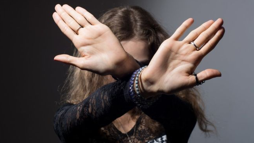 Woman with arms and hands stretched out covering her face