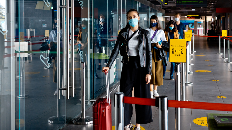 Travellers stand in airport line wearing face masks