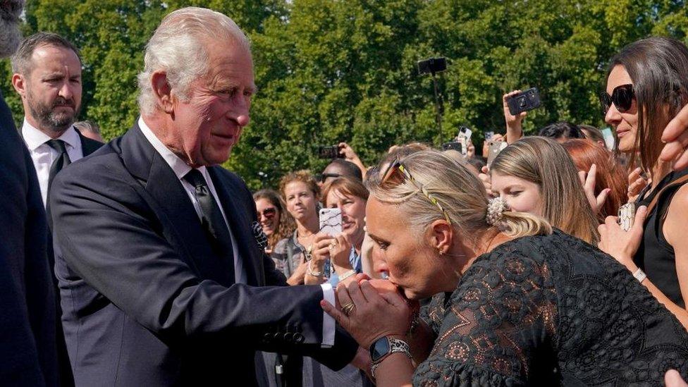 A woman kisses King Charles's hand