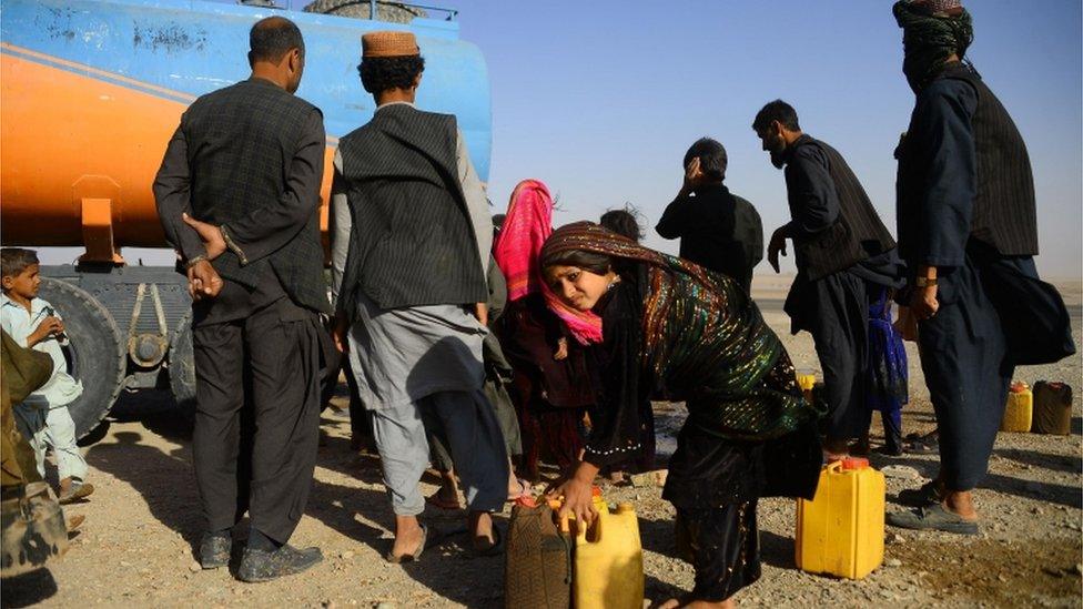 In this photo taken on August 3, 2018, drought-displaced Afghan people fill water containers from a tanker at a camp for internally displaced people in Injil district of Herat province