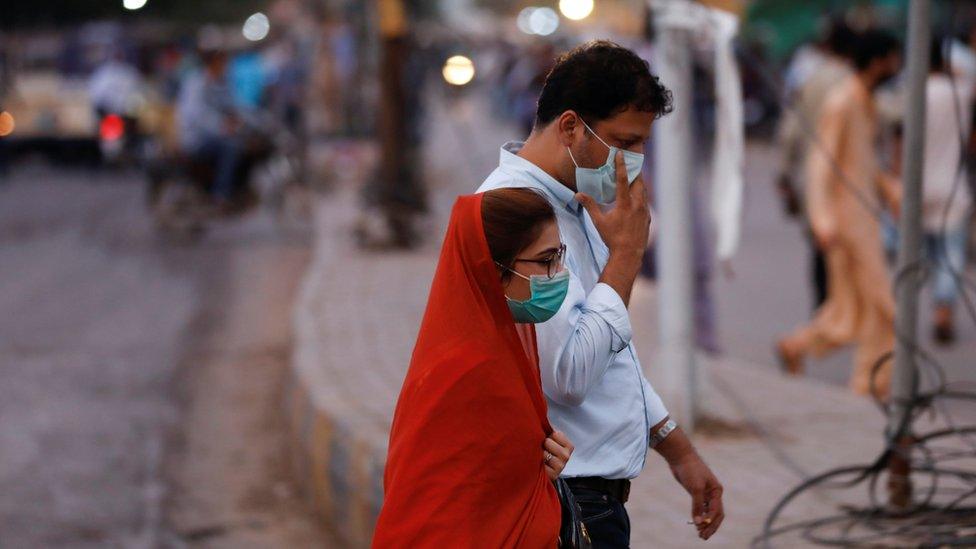 A man and woman wear protective masks while walking along a street after Pakistan lifted lockdown restrictions, as the coronavirus disease (COVID-19) outbreak continues, in Karachi, Pakistan August 18, 2020.