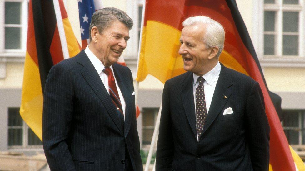 Ronald Reagan and Richard von Weizsaecker stand together in front of American and German flags