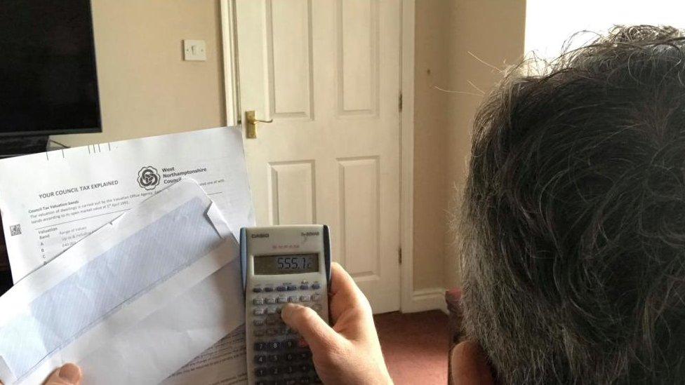 A hand holds up a West Northamptonshire Council Tax bill while another hand holds up a calculator