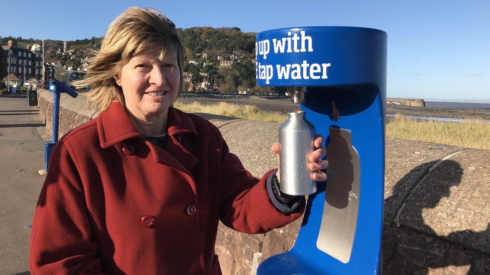 A woman in a red coat filling up a metal water bottle at a stand