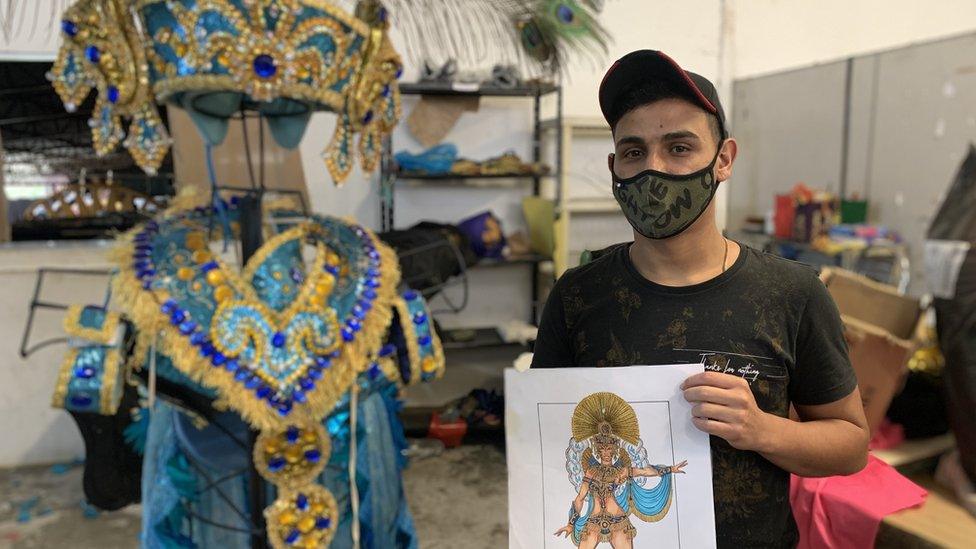 Julio Cesar posing with drawing and one of his elaborate costumes