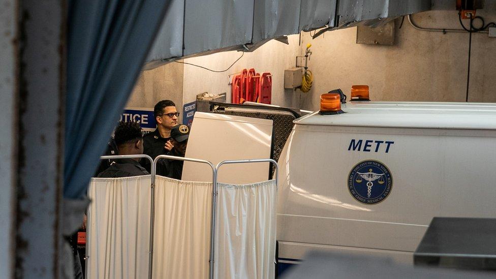 Police officers cover a medical examiner car outside the New York hospital where Epstein was taken to