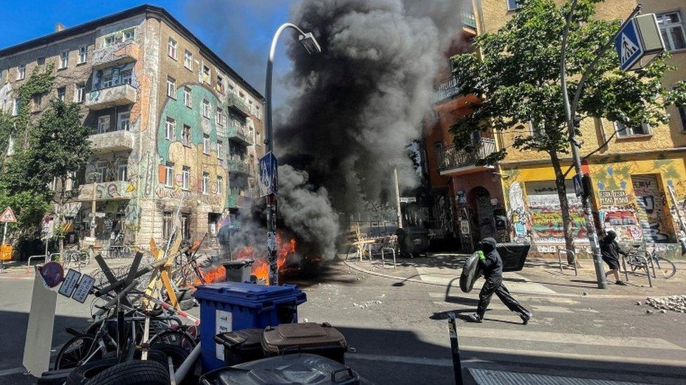 A man holding an object runs toward burning barricades at Rigaer Street in Berlin