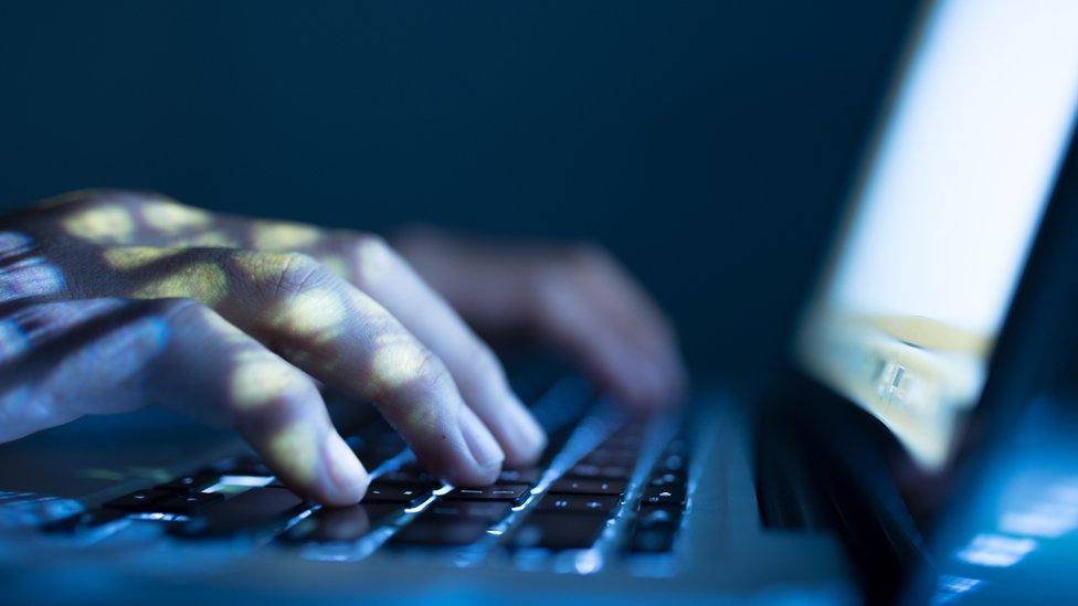 shadowy hands typing on a computer