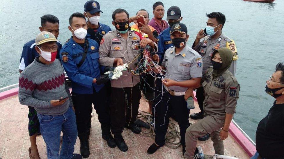 Police officers and fishermen show debris that they believe came from the plane