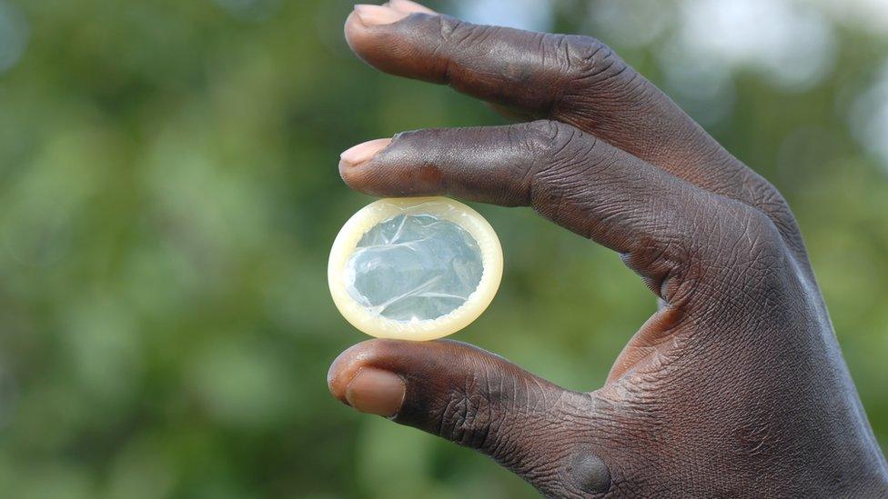 A man holding a condom between his finger and his thumb