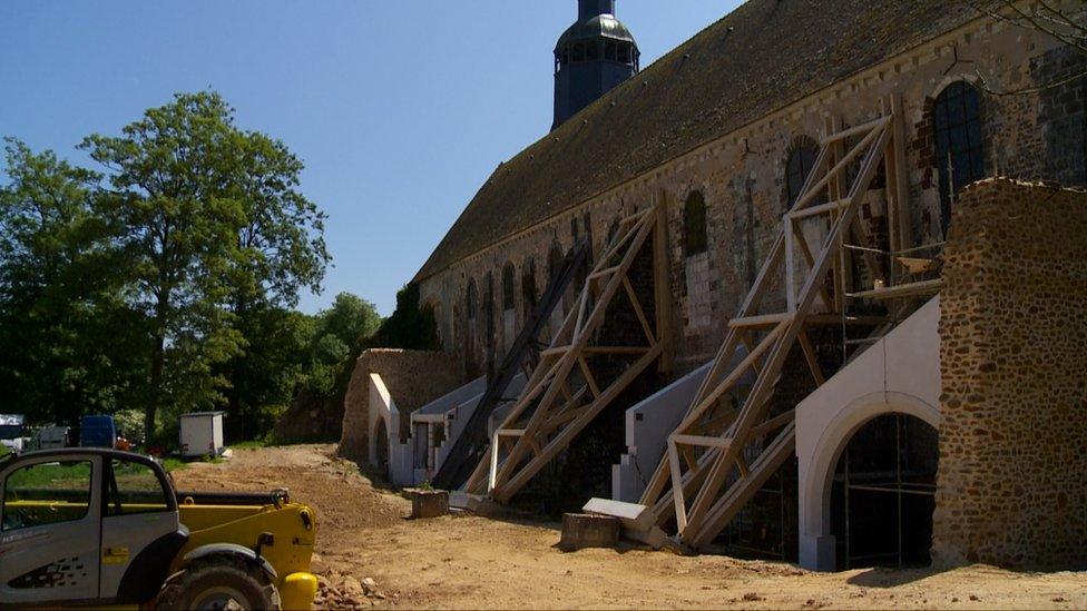 An old church is seen with wooden scaffolding against its walls, clearly holding the building together