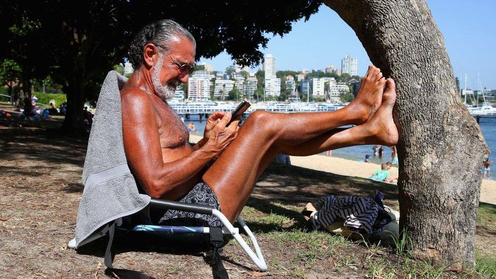 A beachgoer reads his phone in the sun in Sydney, January 2019