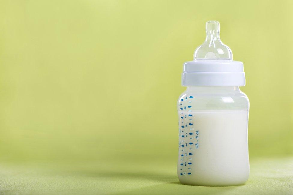 A bottle of formula milk against a green background