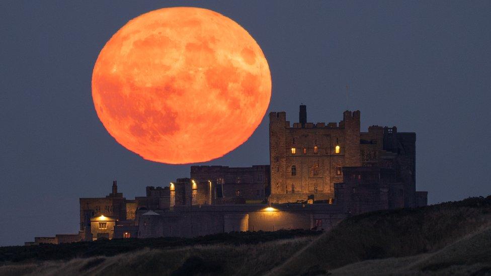 A large orange moon next to a castle