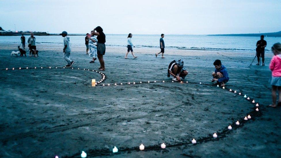 People on a beach next to a heart made of candles