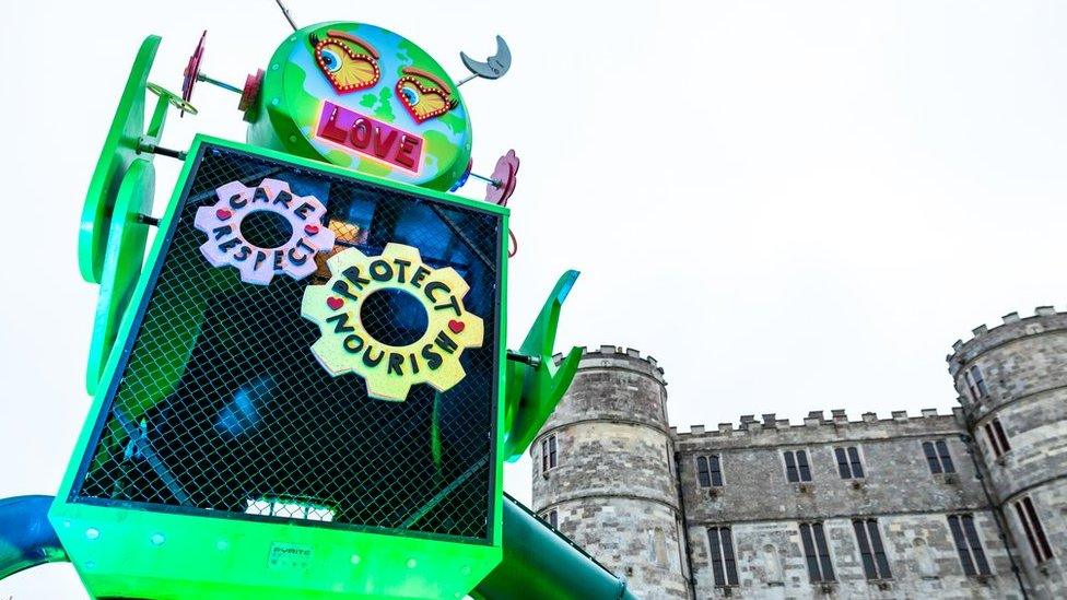 A green robot in front of Lulworth Castle