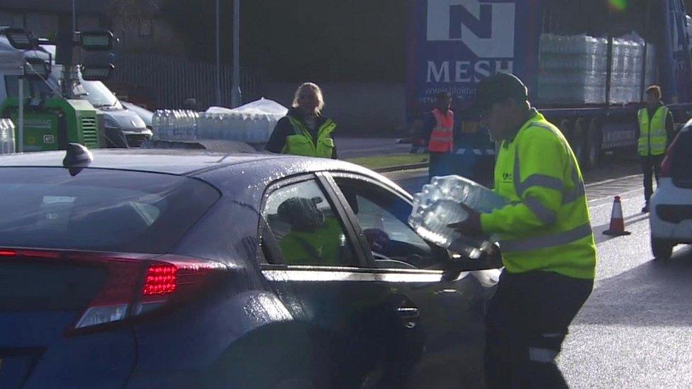 Man handing out bottled water to driver of a car