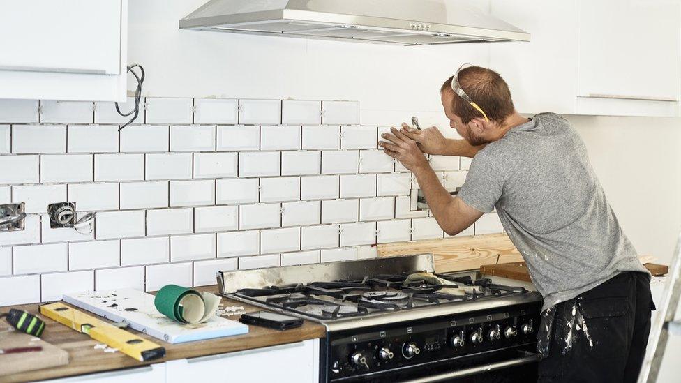 A man working in a new kitchen, a tiler applying tiles to the wall behind the cooker. - stock photo