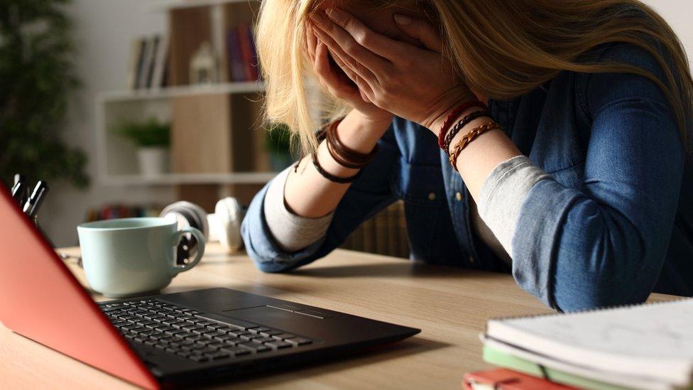 Stock image of a sad woman head in hands in front of a laptop