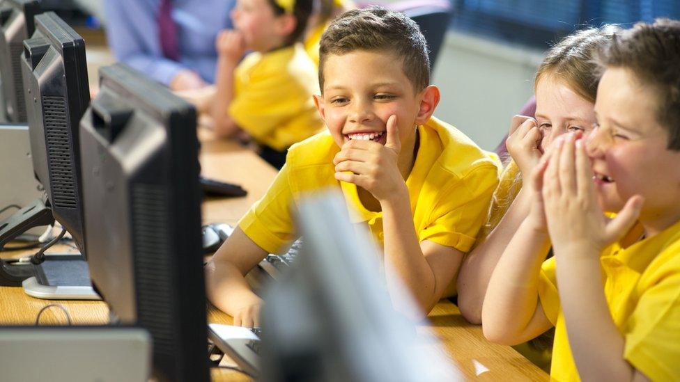 Boys in yellow laughing as they look at computer screens