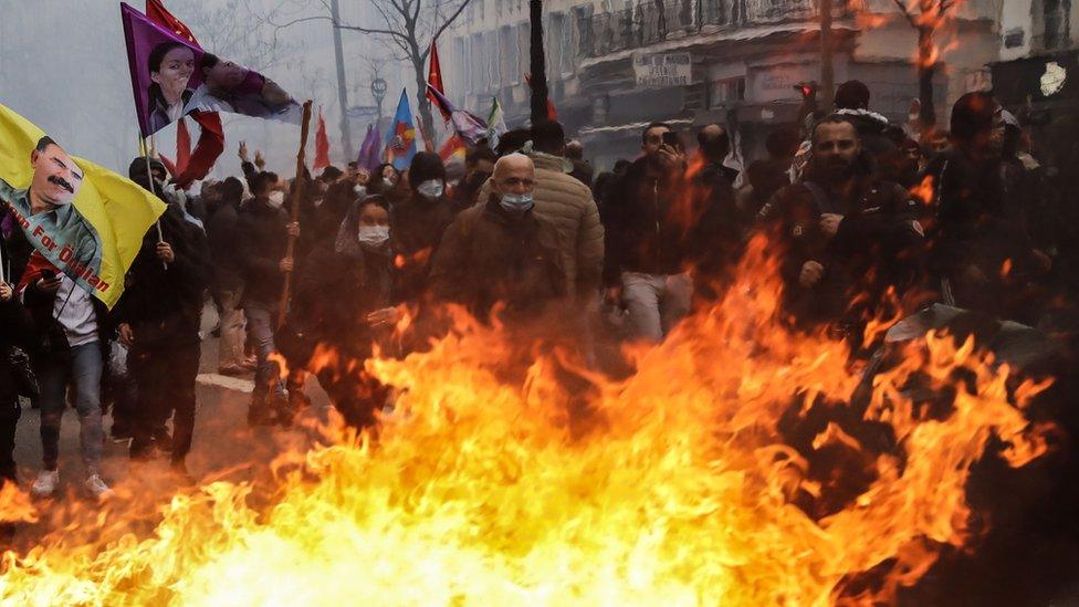 Kurdish protesters stand near a fire in the street in Paris