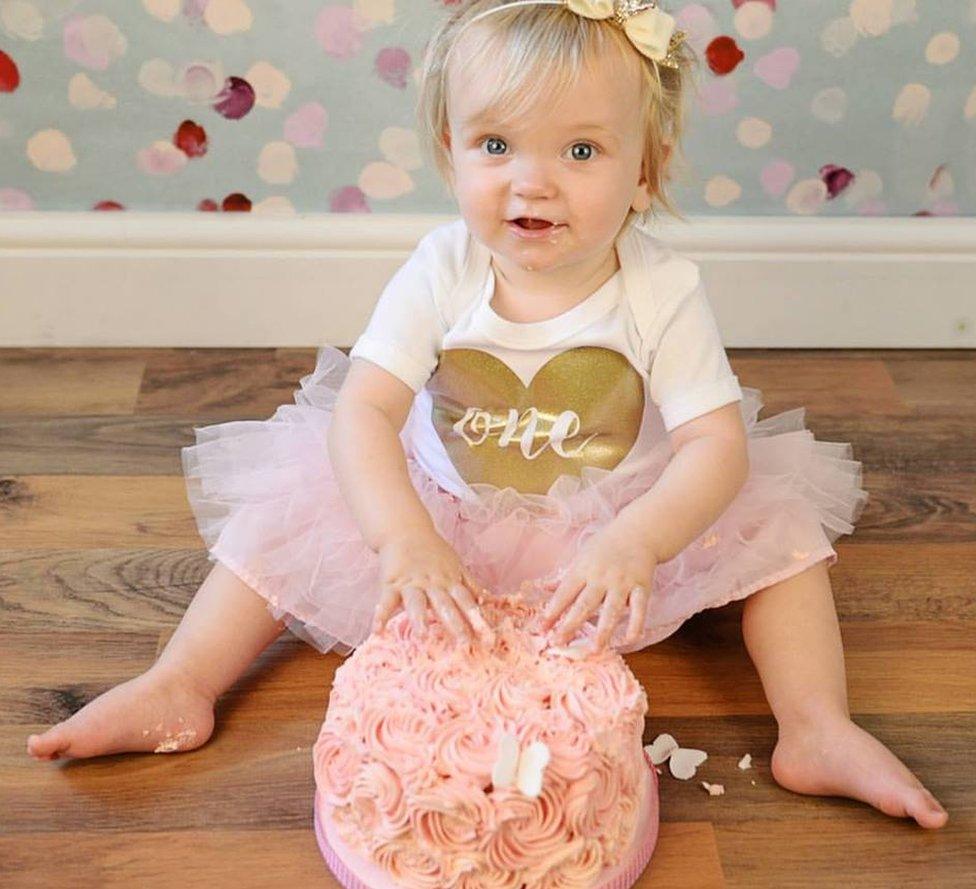 One-year-old Autumn Eden, wearing a pink tutu, sticks her fingers into a pink cake