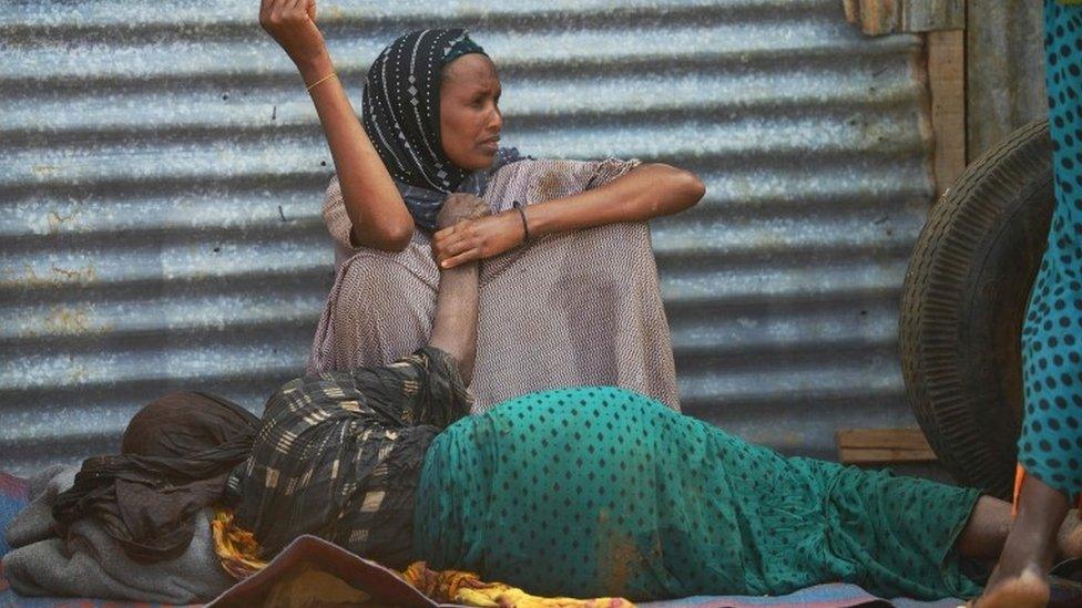 An elderly woman weakened by hunger lies on the ground as her daughter watches over her at a camp for the internally displaced on the outskirts of Baidoa town, the capital of Bay region of south-western Somalia