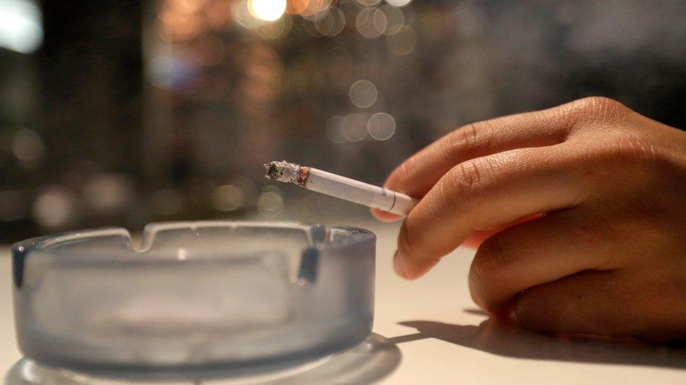 Smoker holding a cigarette over an ashtray