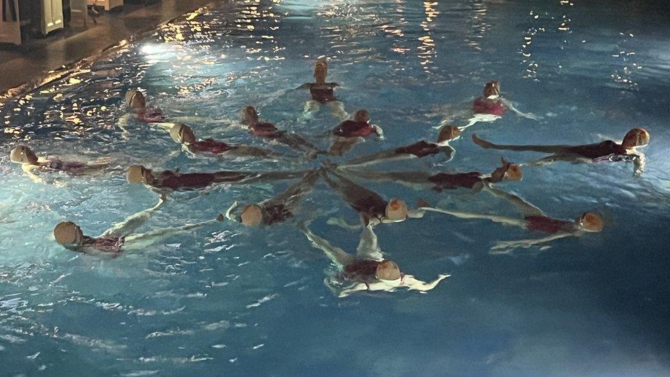 A group of synchronised swimmers in the shape of a snowflake