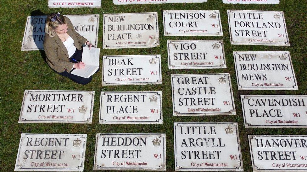 Woman sits with old London street signs