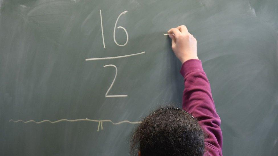 Close crop of a schoolgirl facing a visible classroom chalkboard performing basic maths