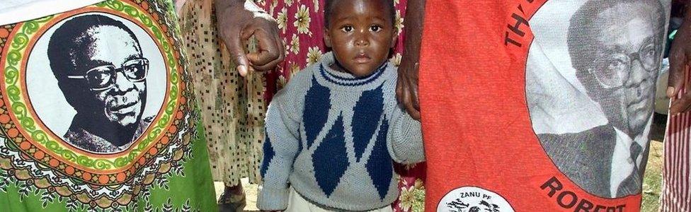 A boy stands between his mother and another Zimbabwe's ruling Zanu PF party supporter wearing skirts displaying Zimbabwean President Robert Mugabe pictures during a rally in the Chitungwiza township south of Harare, 30 April 2000.