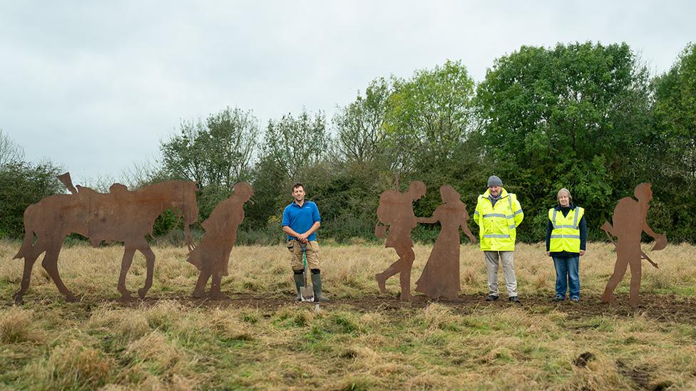 Volunteers stand next to sculptures