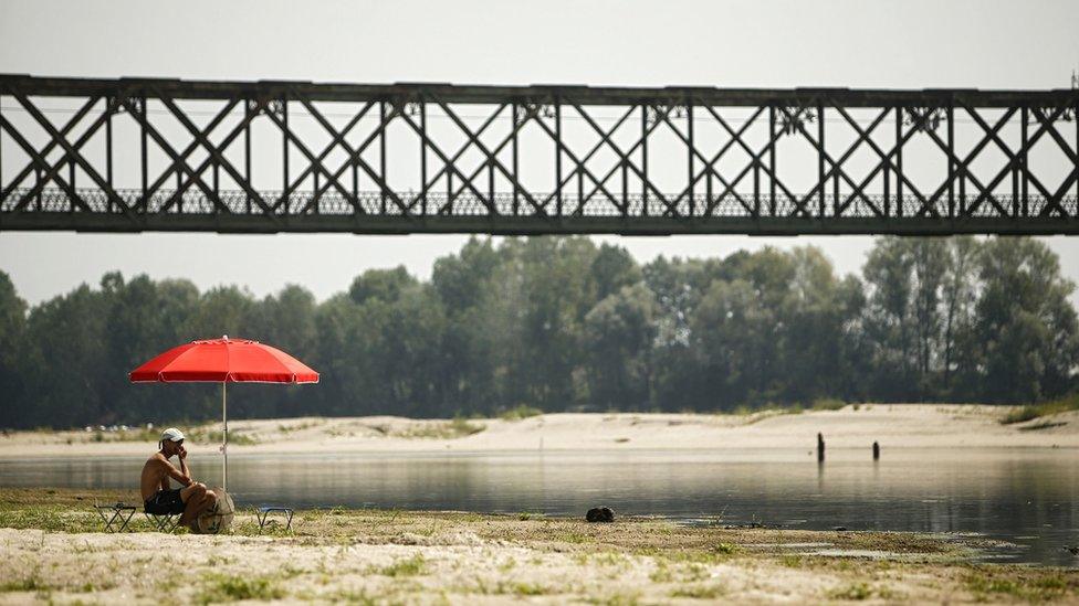 A young man sits under an umbrella at the Po River near the Ponte della Becca bridge in Linarolo, near Pavia, northern Italy