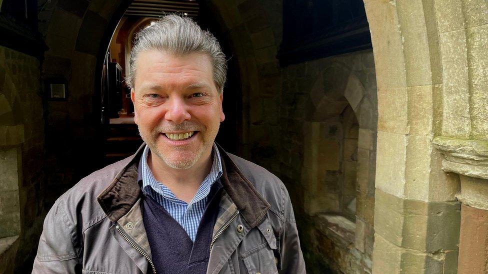 Man with short beard stands in doorway of church