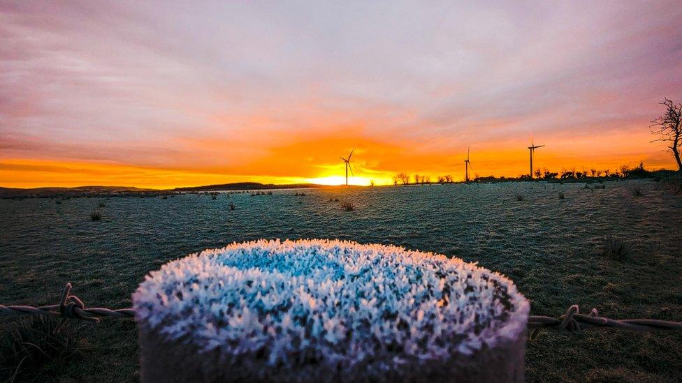 Orange sunrise with a wooden post in the foreground covered in hoar frost