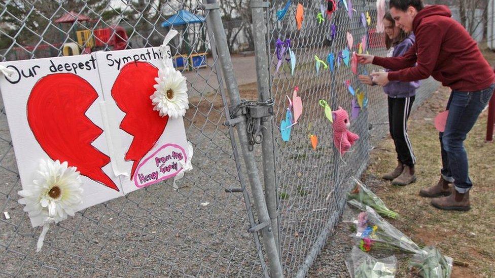 : A woman and her daughter place a heart on a fence at a growing memorial in front of the Debert School April 20, 2020