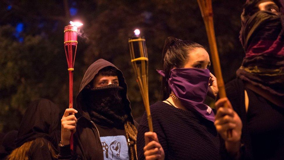 Women covering their faces with black scarves demonstrate, carrying torches