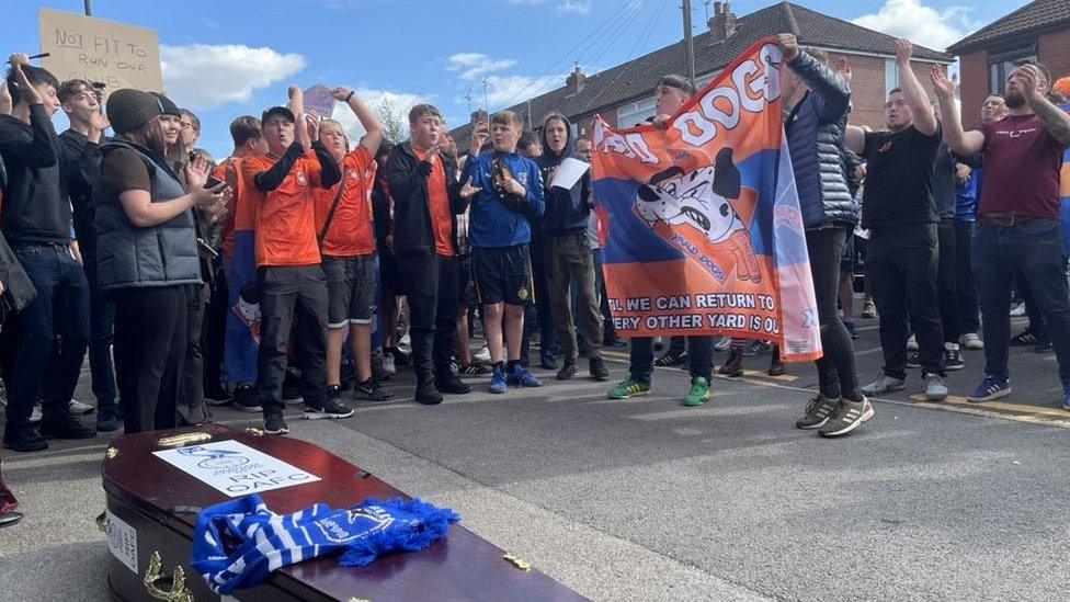 Fans protest behind a mock coffin