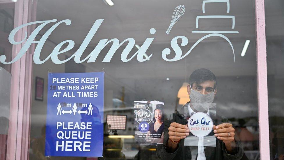 Chancellor of the Exchequer Rishi Sunak places an Eat Out to Help Out sticker in the window of a business during a visit to Rothesay on the Isle of Bute, Scotland.