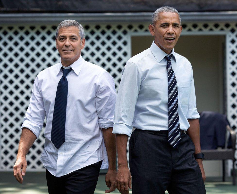 George Clooney, left, and Barack Obama, right, stand back-to-back with shirtsleeves rolled up and top buttons undone.