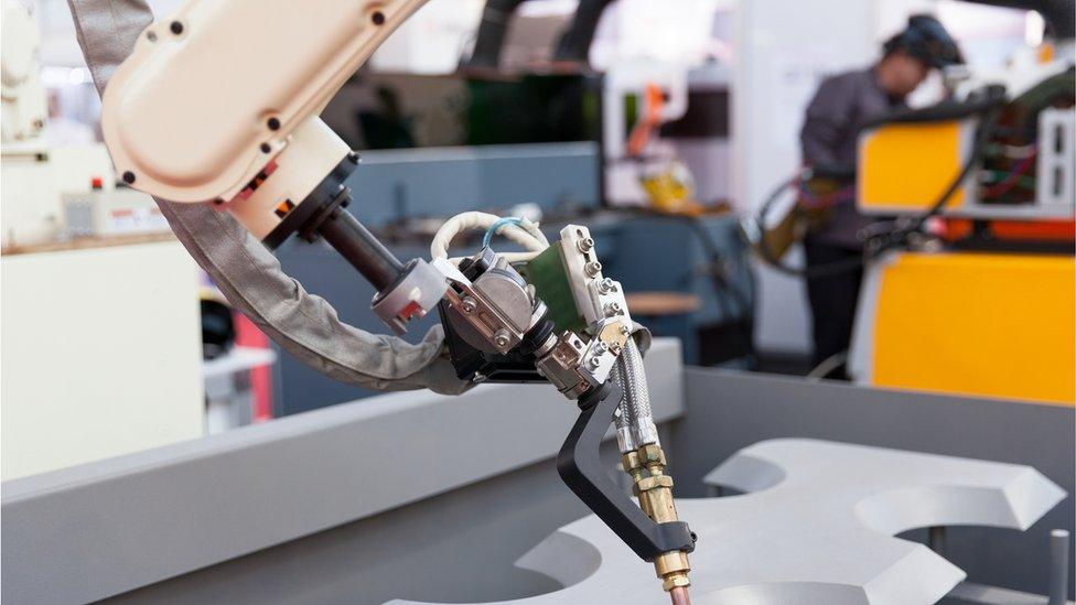 A robot arm works on a car, alongside a factory worker