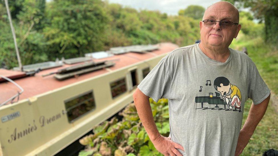 Widowed pensioner, Phil Hatfield, standing with his hands on his hips next to his boat "Annie's Dream"