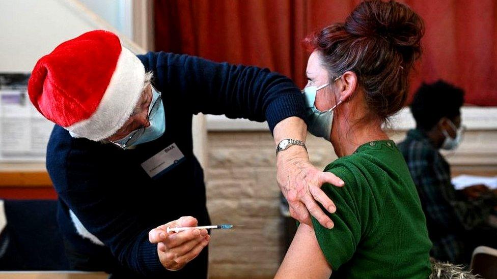 Woman receiving Covid vaccination at centre from medic wearing a Santa hat