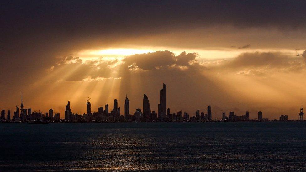 kuwait city skyline silhouetted against a sun peaking through the clouds