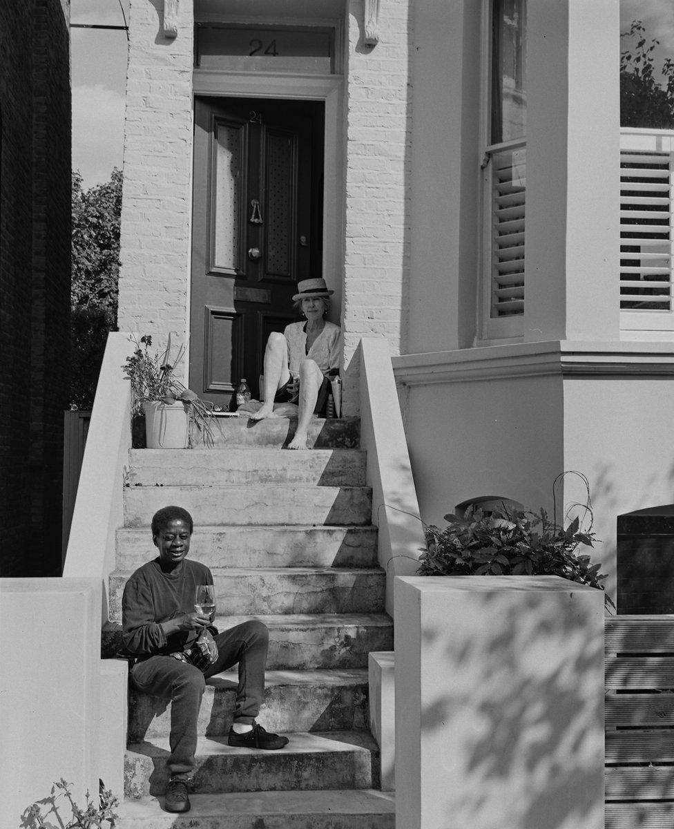 Two people sit on the steps of a residential building drinking together